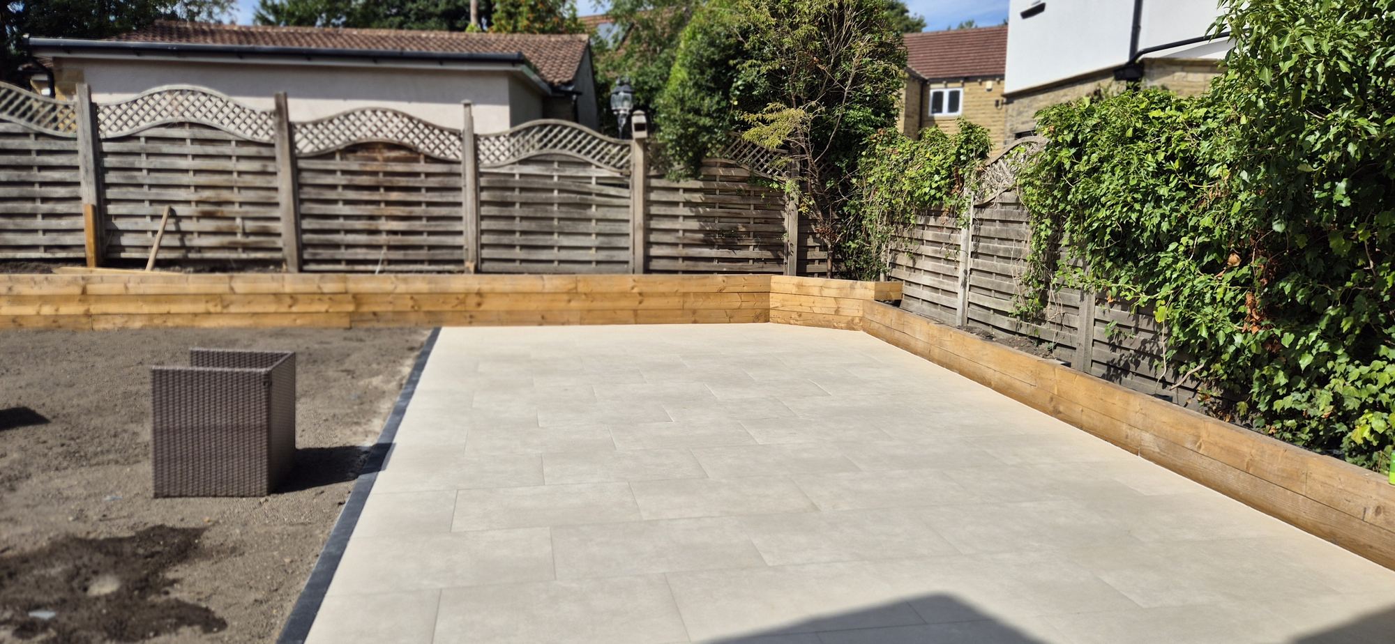 finished cream porcelain patio with sleeper-edged beds, the garden topsoiled ready for turf