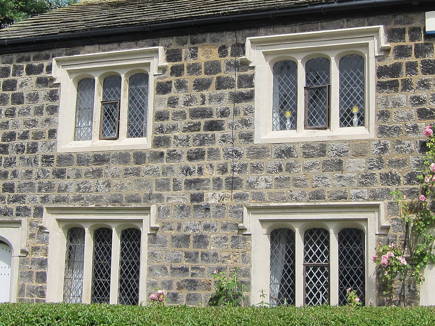 gritstone cottage wall in Leeds, coursed dark stone with pale dressed window surrounds