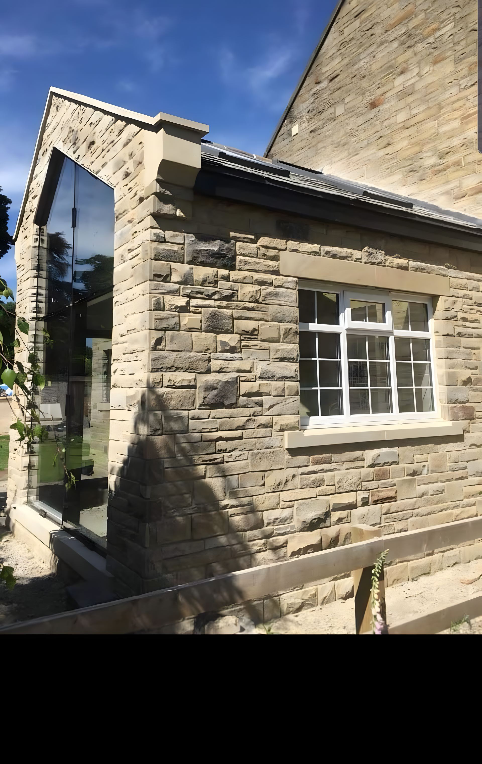 Reclaimed stone coursing built up around a glazed gable on a two storey extension