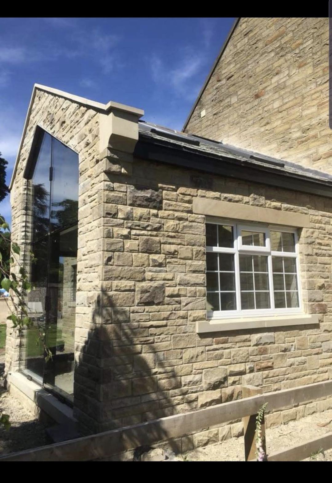 a finished extension corner in stone, frameless glazed gable above