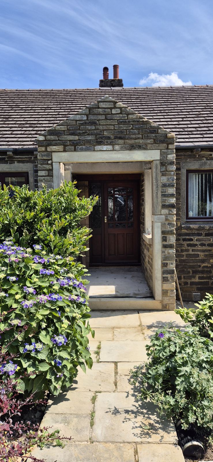 Stone built porch with a dressed stone surround and Indian stone flag path