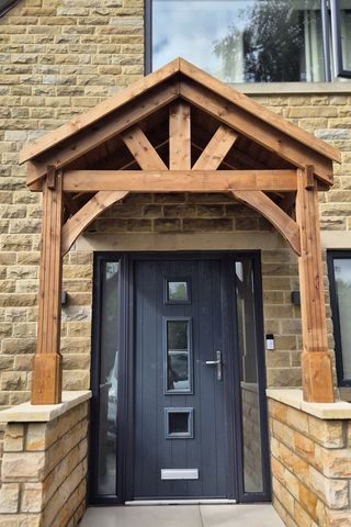 A timber porch canopy over a front door, on stone dwarf walls