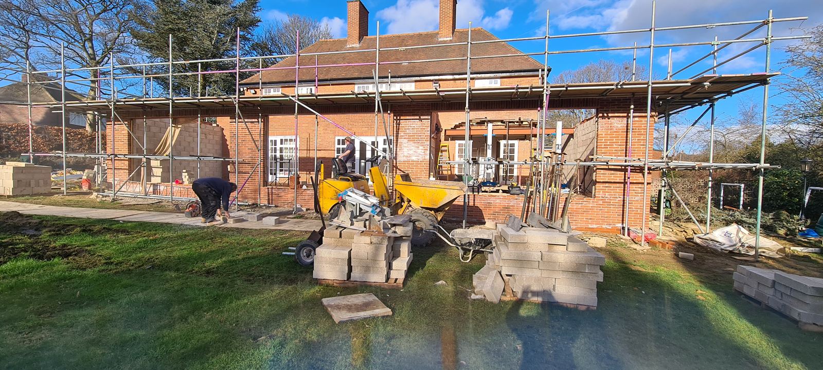 The team at work on a scaffolded extension, stone flags stacked on the lawn